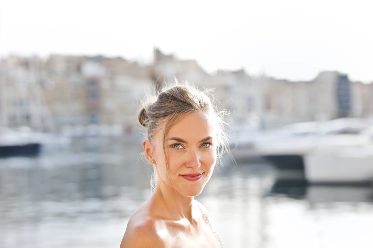 A smiling woman by the scenic Mgarr harbor in Malta, enjoying a sunny day.