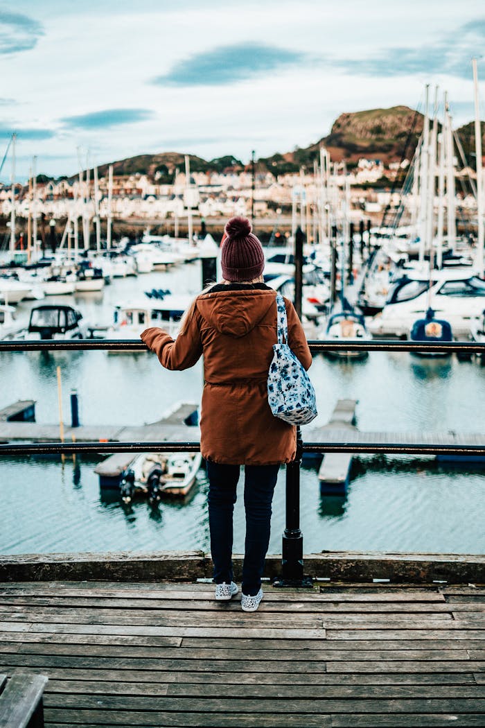 A woman stands on a wooden dock overlooking a scenic marina filled with boats in Wales.