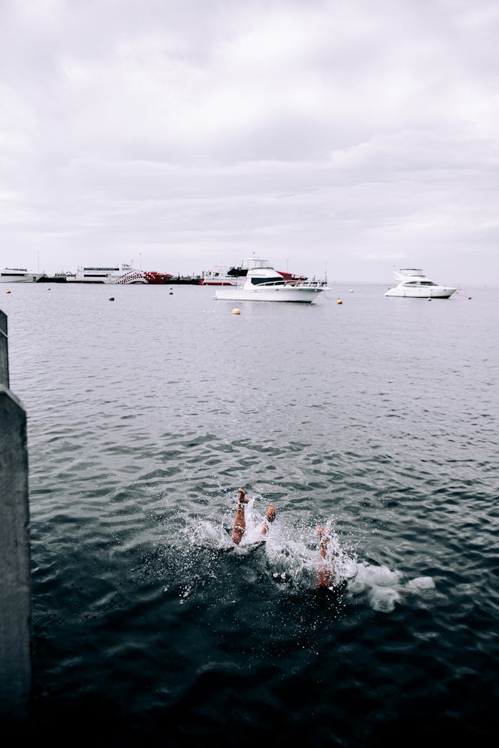 Two people diving into the ocean with yachts moored under an overcast sky. Captured with a Canon EOS 6D.